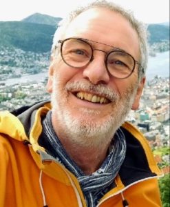Selfie von Klaus Arabin in gelbem Anorak mit der Stadt Oslo im Hintergrund. Trägt eine Brille und einen grauen Drei-Tage-Bart